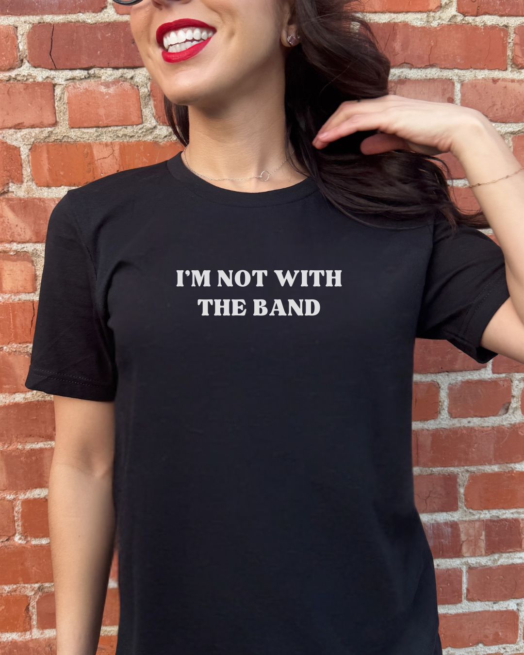 Person wearing a black t-shirt with 'I'm not with the band' text against a brick wall.