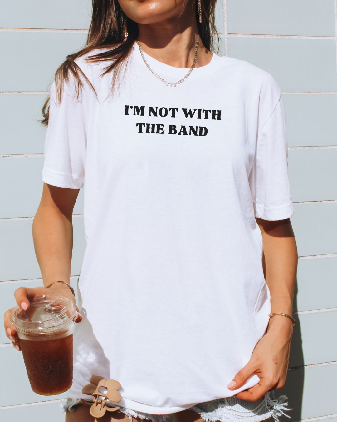 Person wearing a white t-shirt with 'I'm not with the band' text, holding a drink.