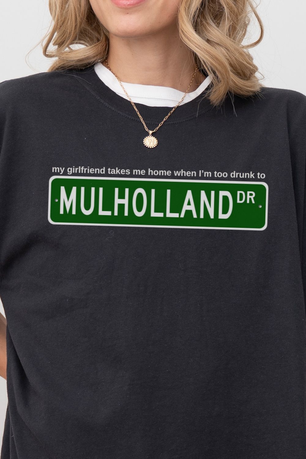 black t-shirt with Mulholland Drive street sign design on a white background, with blink 182 lyrics my girlfriend takes me home when I'm too drunk to drive, worn by a person