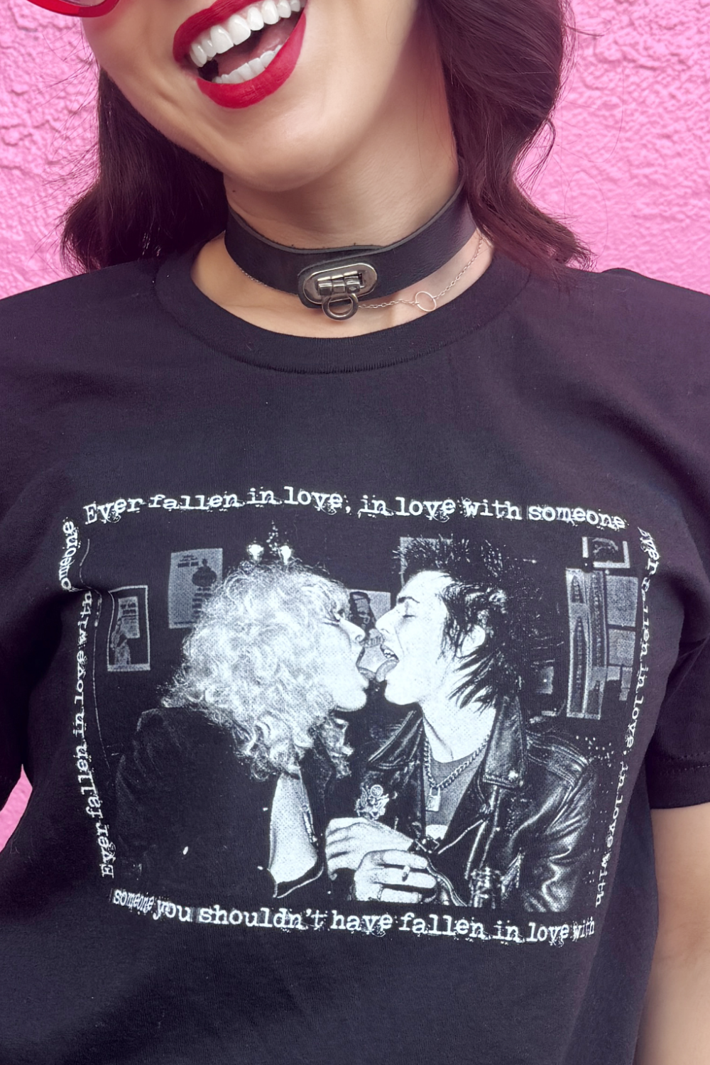 Person wearing a black t-shirt with a 70s punk graphic design and text, against a pink background.