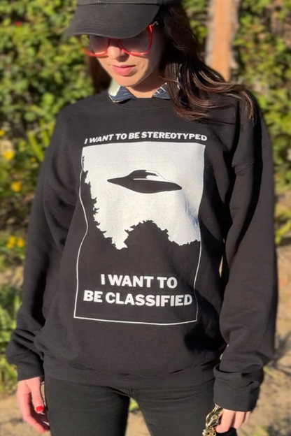 Person wearing a black sweatshirt with a graphic design and text outdoors.